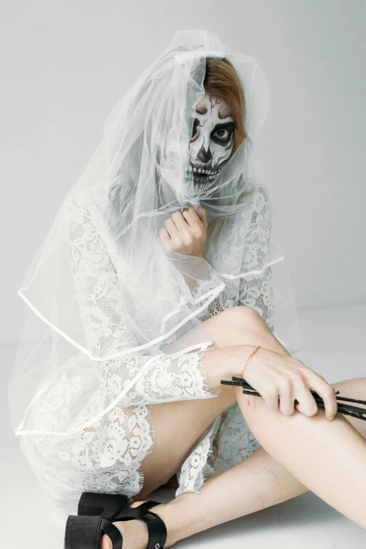 a woman sitting on the floor with a knife in her hand, an album cover, inspired by Elsa Bleda, trending on pexels, gothic art, wearing a wedding dress, skull face paint, white transparent veil, ( ( ( skeleton ) ) )