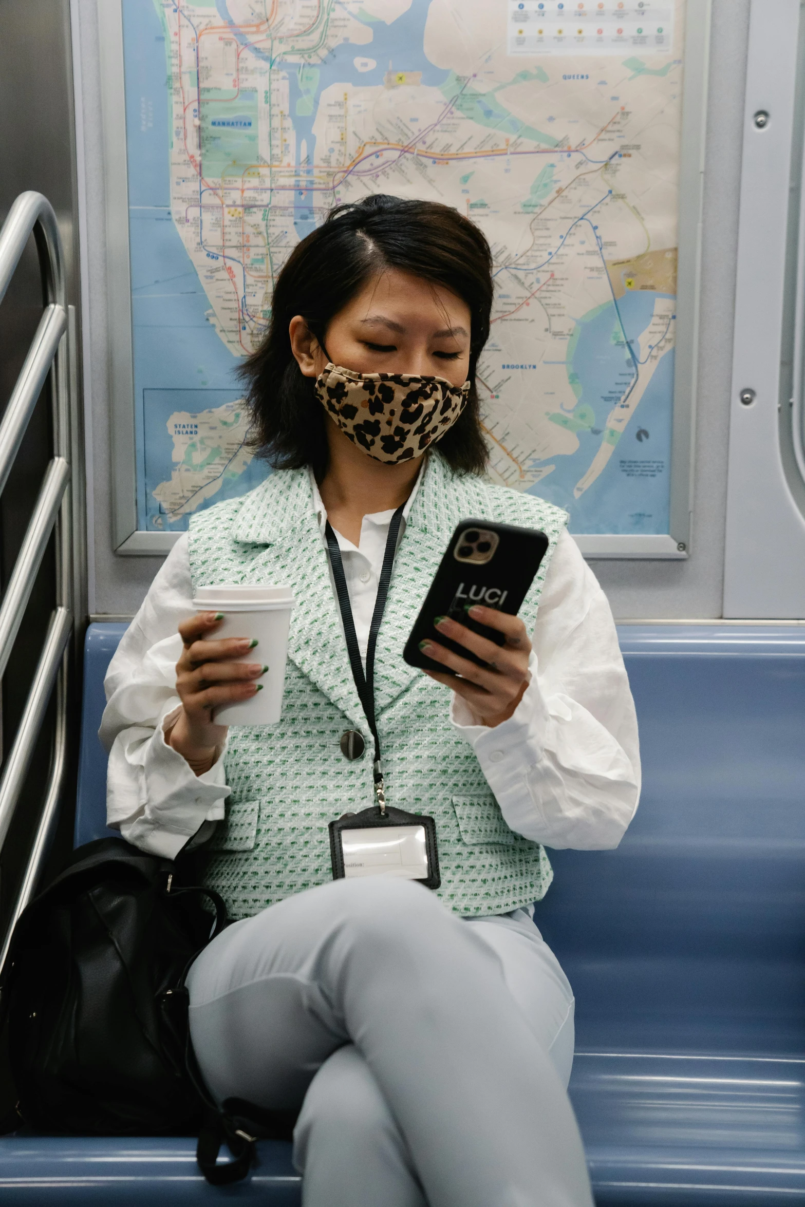 a woman sitting on a train looking at her cell phone, wearing bandit mask, in new york, lulu chen, green facemask