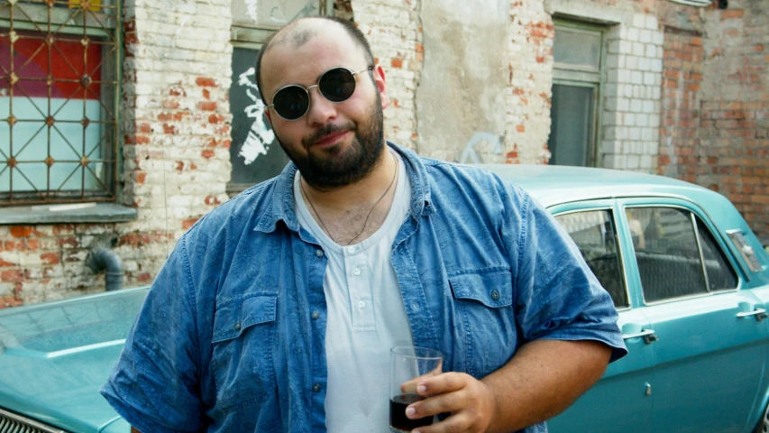 a man standing in front of a car holding a drink, an album cover, by Attila Meszlenyi, pexels contest winner, photorealism, plus-sized, neckbeard, hasbulla magomedov, balding