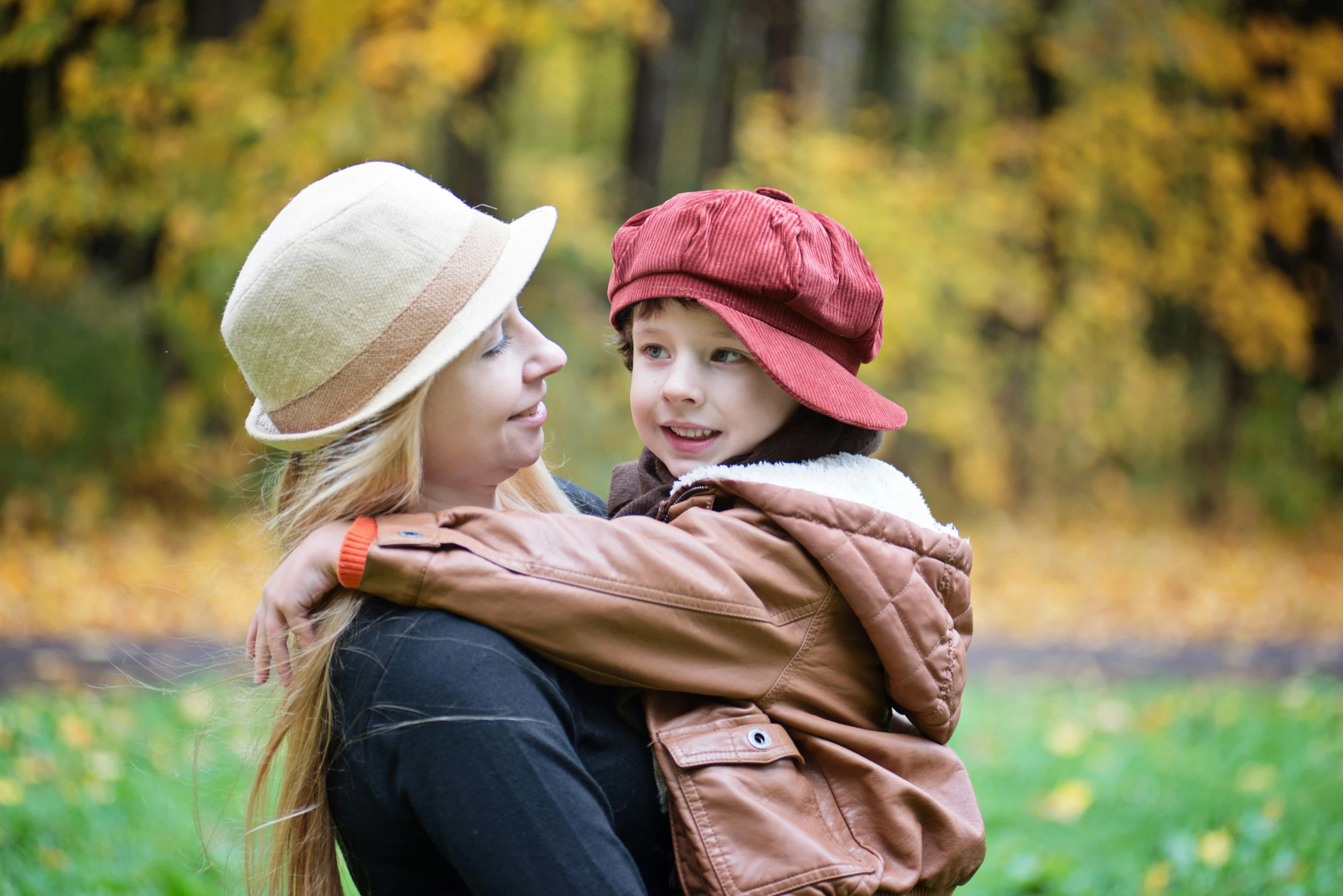 a woman holding a child in her arms, a picture, inspired by Kate Greenaway, shutterstock, caracter with brown hat, grassy autumn park outdoor, leather clothing, 15081959 21121991 01012000 4k