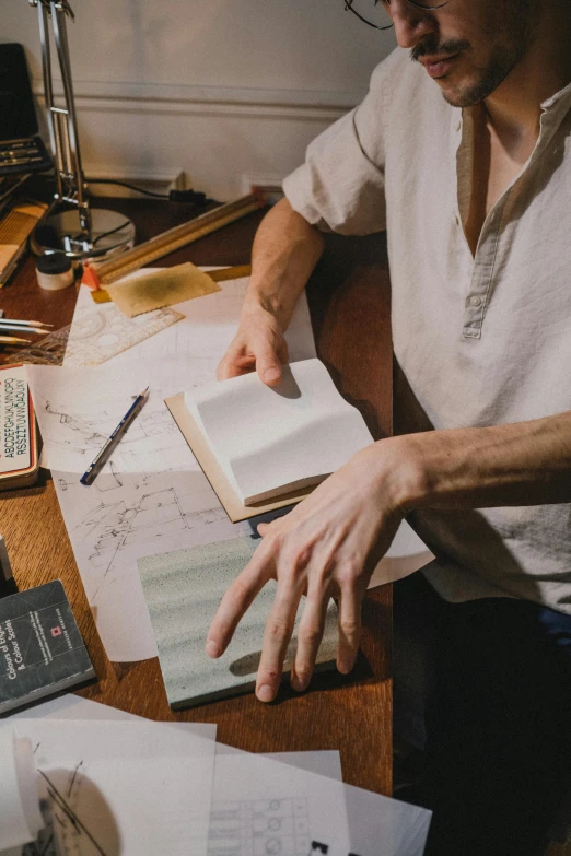 a man that is sitting at a table with a book, a drawing, pexels contest winner, arts and crafts movement, ignant, hands on counter, sydney hanson, cartographic