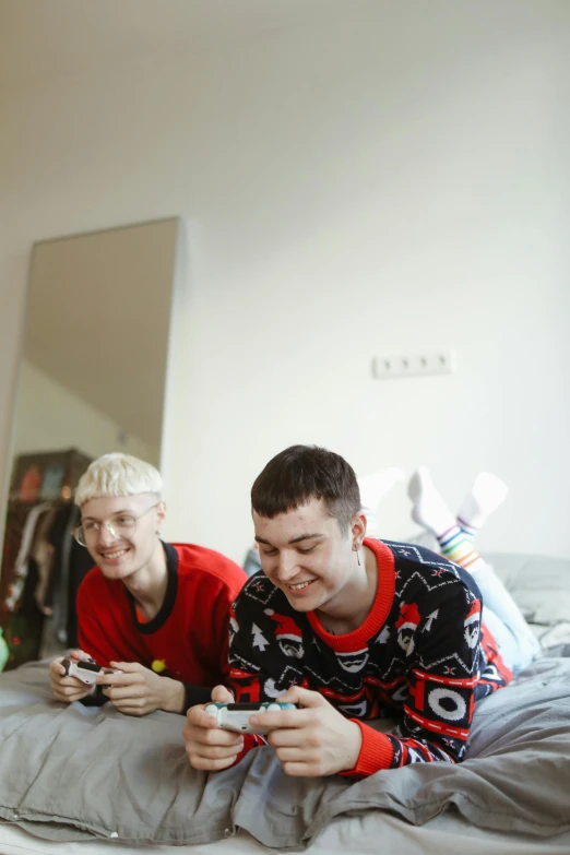 a couple of men laying on top of a bed, by Matija Jama, playing video games, pale hair, non-binary, high resolution photo