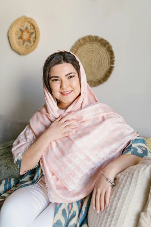 a woman sitting on a couch wearing a pink scarf, inspired by Maryam Hashemi, hurufiyya, pastel pink skin tone, wearing simple robes, patterned scarf, thumbnail