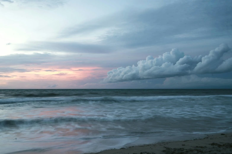 a large body of water sitting on top of a sandy beach, an album cover, pink and grey clouds, sri lanka, overcast dawn, ignant
