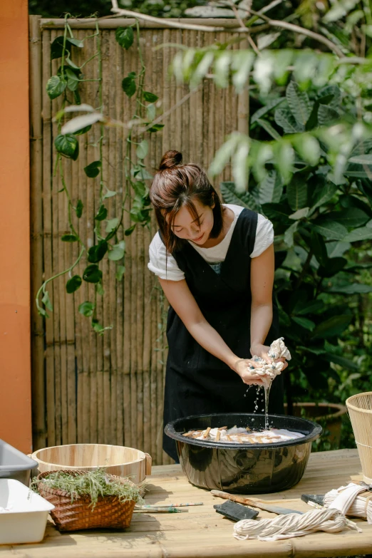 a woman pouring something into a bowl on a table, a portrait, inspired by Nishida Shun'ei, unsplash, outdoor, cooking show, fountain, over-shoulder shot