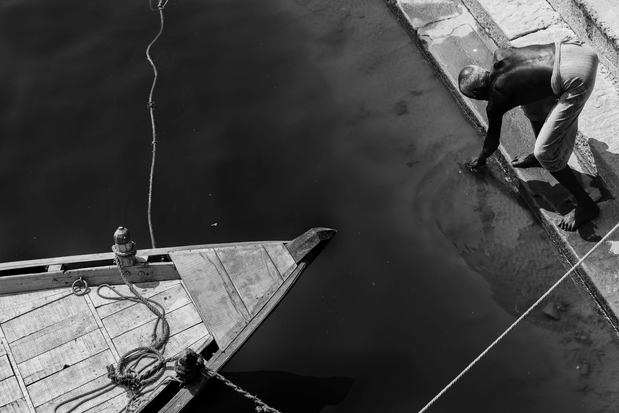 a man standing next to a boat on a body of water, a black and white photo, by Ibrahim Kodra, pexels contest winner, a high angle shot, floating power cables, working, small dock