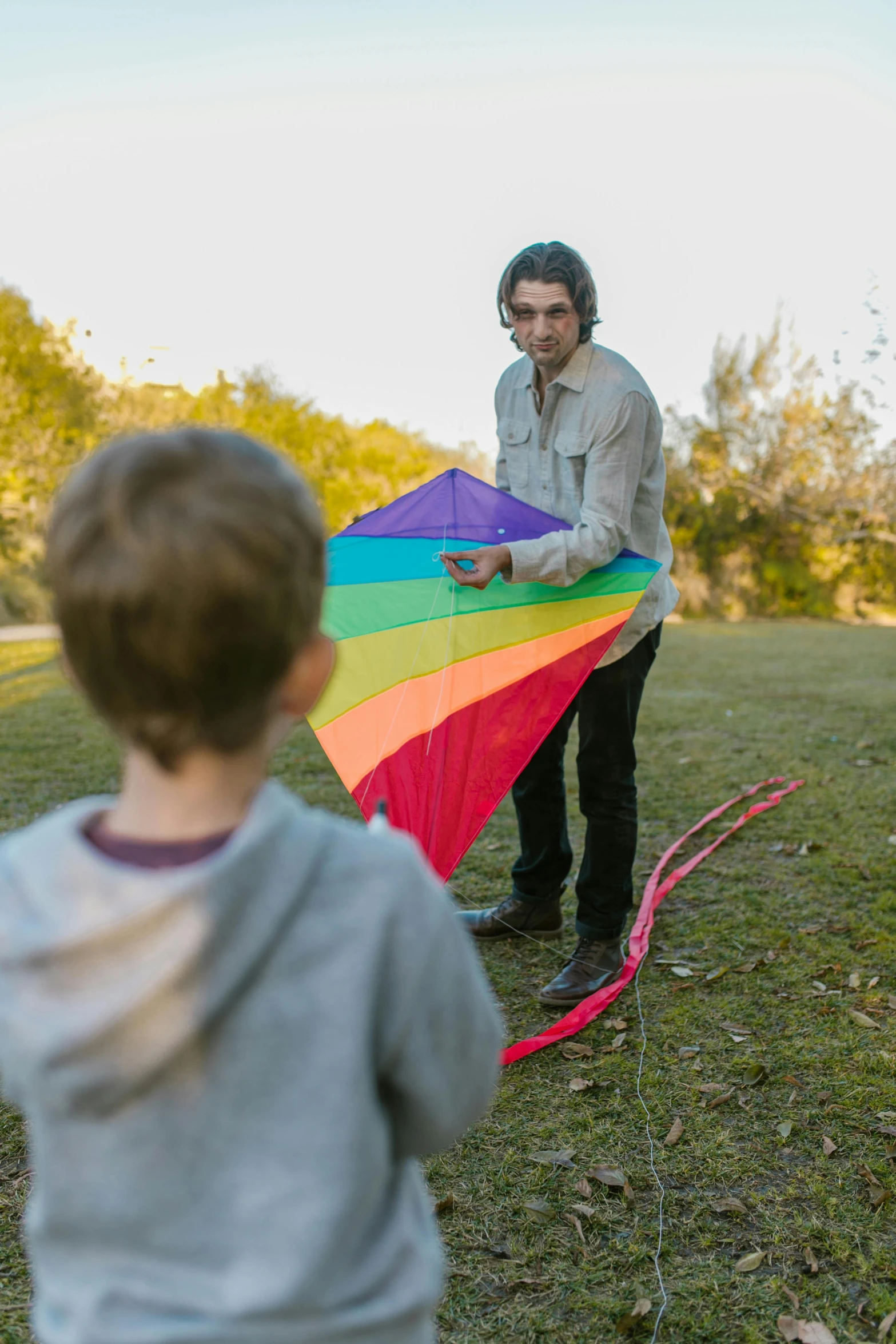 a man standing next to a little boy holding a kite, sydney park, rainbow wings, profile image, production still