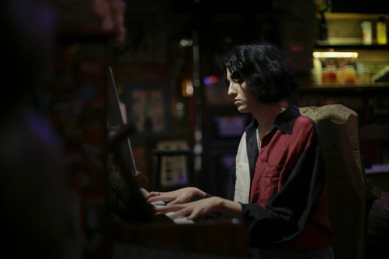 a man sitting in front of a laptop computer, an album cover, pexels, serial art, finn wolfhard, dimly lit dive bar, attractive male playing piano, with his long black hair