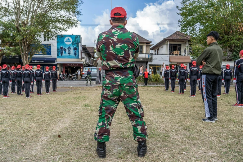 a group of men standing on top of a grass covered field, inspired by Oka Yasutomo, pexels contest winner, hurufiyya, wearing a red captain's uniform, standing in township street, jungle camo, symmetrical image