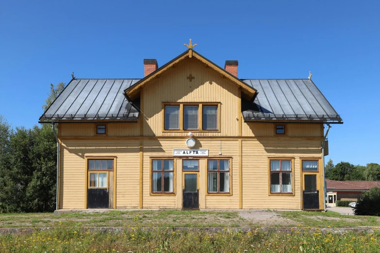 a yellow house sitting on top of a lush green field, by karlkka, train station, stone runes on the front, taiga, symmetrical details