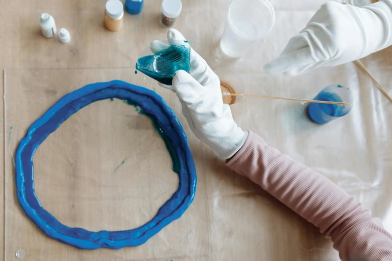 a close up of a person painting on a table, inspired by Otto Piene, trending on pexels, shaped like torus ring, prussian blue, clay material, cast glass