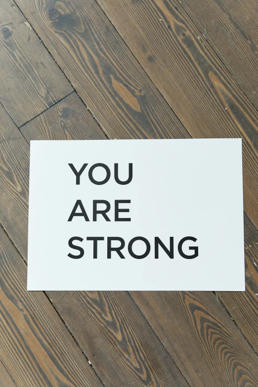 a sign that says you are strong on a wooden floor, a screenprint, by Julia Pishtar, dada, at home, kanye, minimalist sticker, white