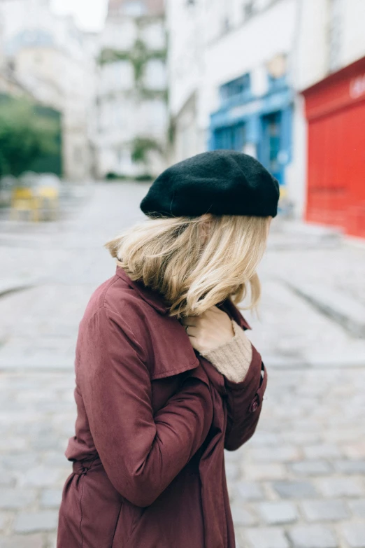 a woman standing in the middle of a street, inspired by Albert Paris Gütersloh, trending on pexels, wearing a beret, shy looking down, a blond, maroon