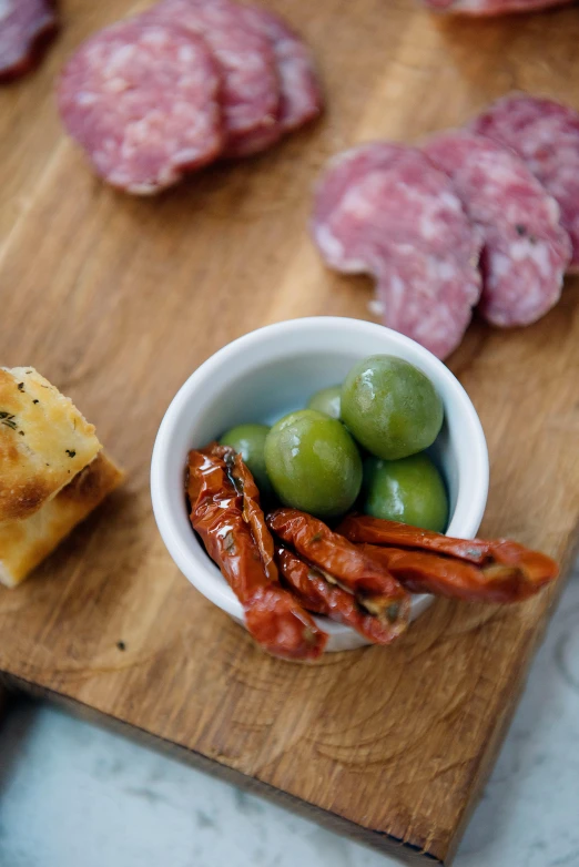 a wooden cutting board topped with different types of food, olives, offering a plate of food, salami, handheld