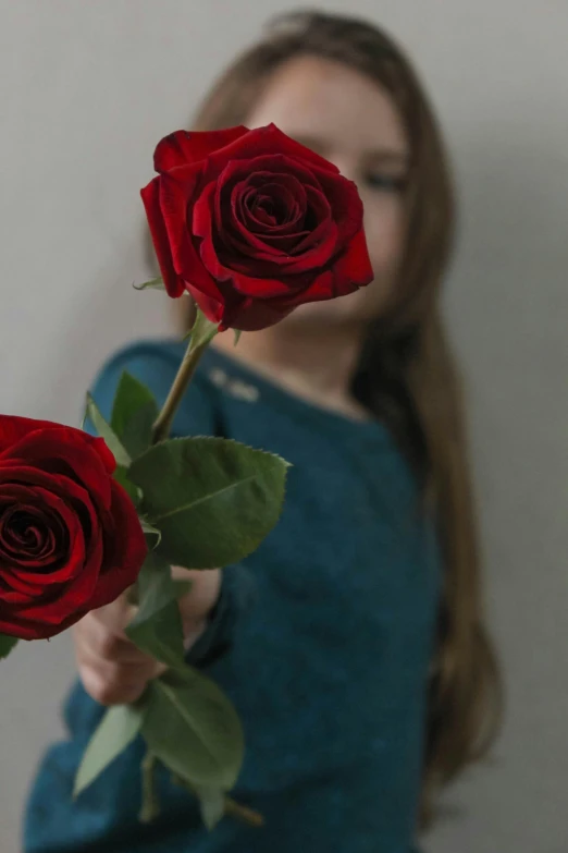 a woman holding two red roses in front of her face, pexels contest winner, 4yr old, on a gray background, profile pic, blue or red