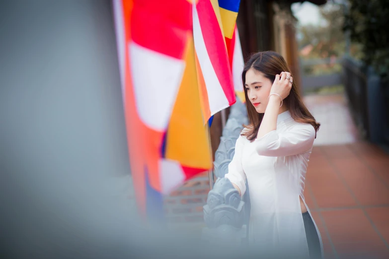 a woman standing in front of a bunch of flags, inspired by Cui Bai, pexels contest winner, white sleeves, vietnamese woman, looking around a corner, elegant look