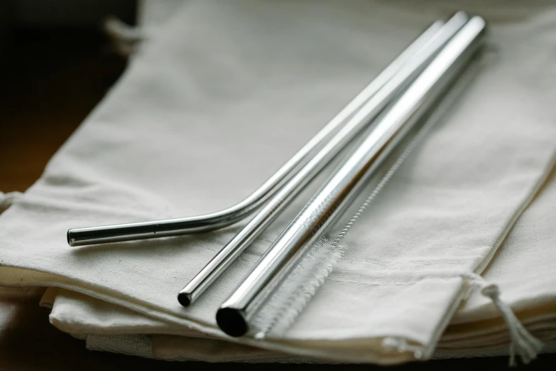 two metal straws sitting on top of a napkin, unsplash, pouches, liquid polished metal, traditional medium, 3 - piece