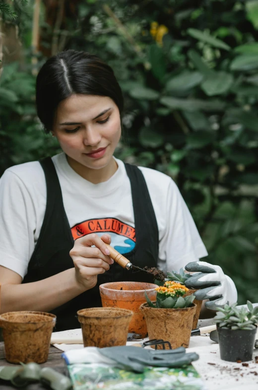 a woman sitting at a table with potted plants, pexels contest winner, wearing a tee shirt and combats, carving, malaysian, gif