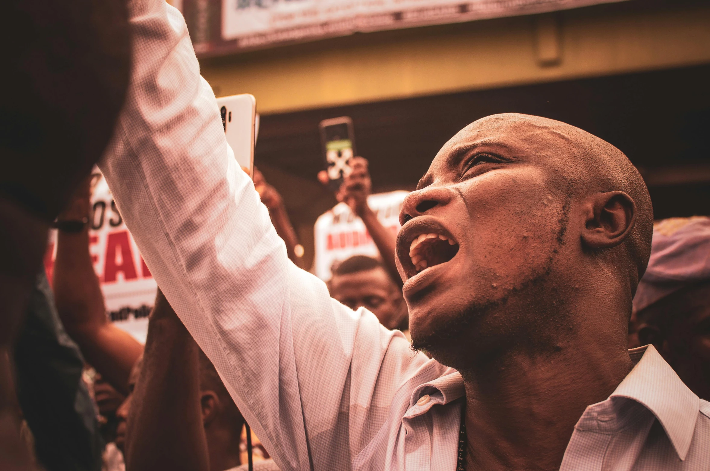 a man holding a cell phone up in the air, by Matija Jama, pexels, renaissance, african aaron paul, protest, portrait of bald, fierce expression