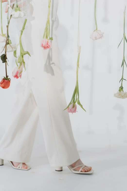 a woman standing in front of a bunch of flowers, by Rebecca Horn, large pants, hanging from white web, detail shot, off - white collection