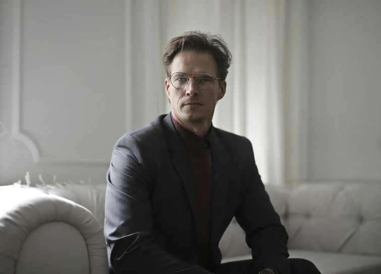 a man in a suit sitting on a couch, a character portrait, inspired by Einar Hakonarson, pexels, bjarke ingels, wearing a suit and glasses, julian ope, portrait image