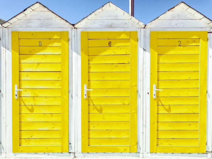 a row of yellow beach huts sitting next to each other, inspired by Wes Anderson, unsplash, sparkling in the sunlight, two wooden wardrobes, white and yellow scheme, wooden toilets