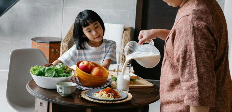 a woman and a child sitting at a table with food, inspired by Yukimasa Ida, pexels contest winner, flowing milk, white apron, longque chen, janice sung