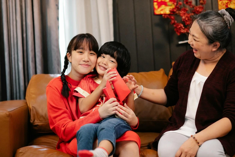 a woman sitting on top of a couch next to a little girl, pexels contest winner, wearing red clothes, asian features, avatar image, smiling playfully