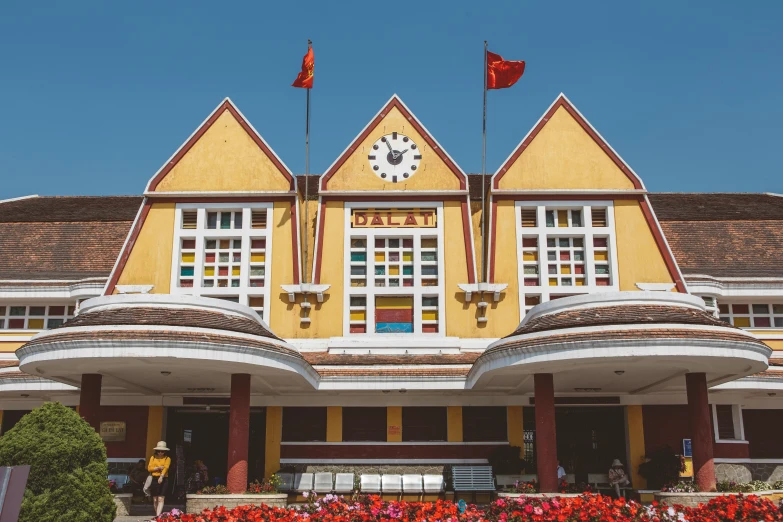 a building with a clock on the front of it, pexels contest winner, yellow and red color scheme, vietnamese woman, train station in summer, 🚿🗝📝