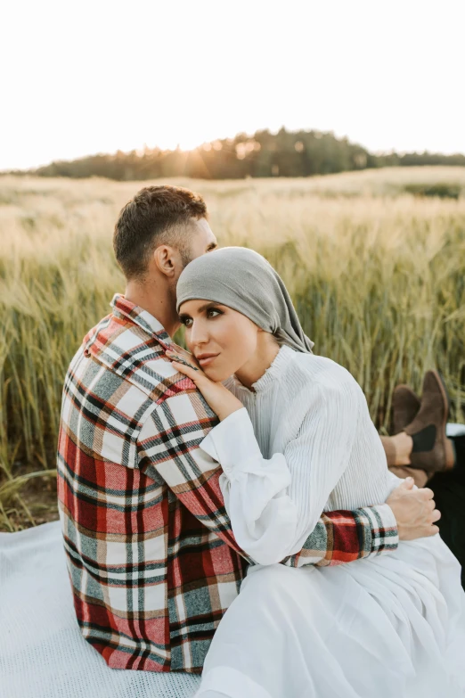 a man and woman sitting on a blanket in a field, a picture, by Julia Pishtar, hurufiyya, wearing beanie, embracing, muslim, no crop