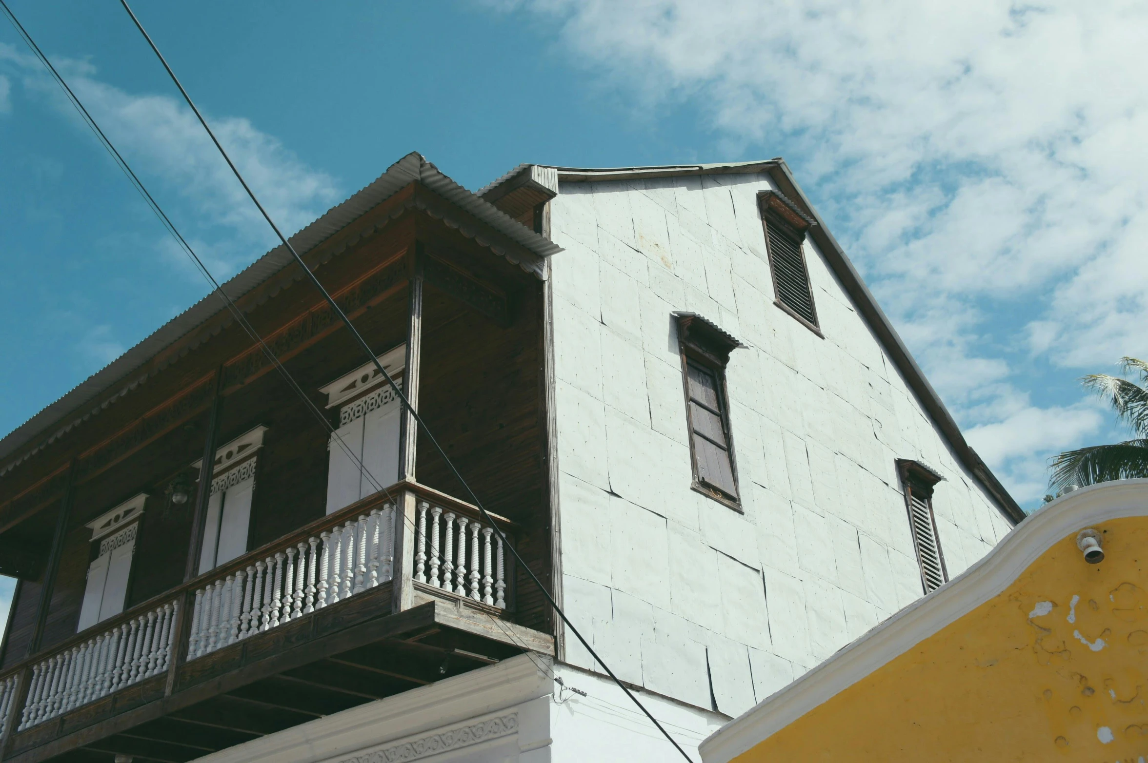 a white and yellow building with a balcony and balconies, an album cover, pexels contest winner, quito school, peaked wooden roofs, helio oiticica, location of a dark old house, low angle facing sky