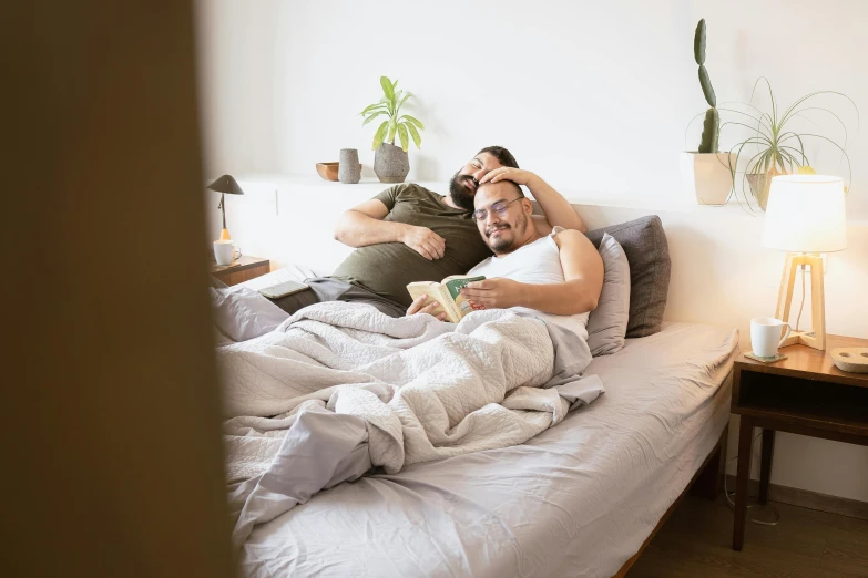 a man laying on top of a bed next to a woman, a photo, lgbtq, reading, australian, happy couple