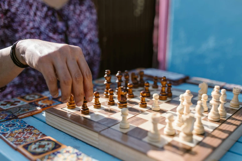 a person playing a game of chess on a table, by Carey Morris, trending on unsplash, al fresco, crafts and souvenirs, 🦩🪐🐞👩🏻🦳, blue checkerboard dress