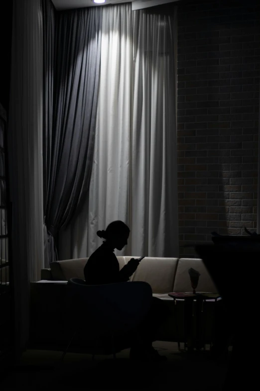 a person sitting on a couch in a dark room, by Shang Xi, silhouette, sitting in a cafe alone, reading, dark drapery