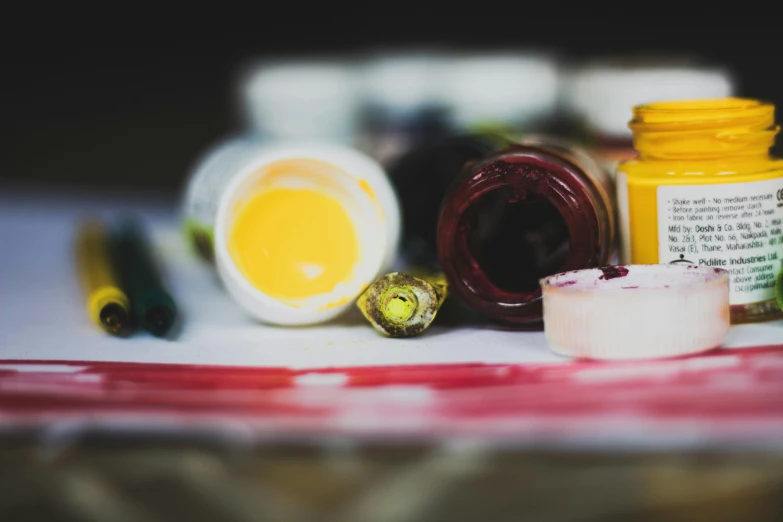 a couple of bottles of paint sitting on top of a table, by Sylvia Wishart, unsplash, yellows and reddish black, inks, painting a canvas, close up photograph
