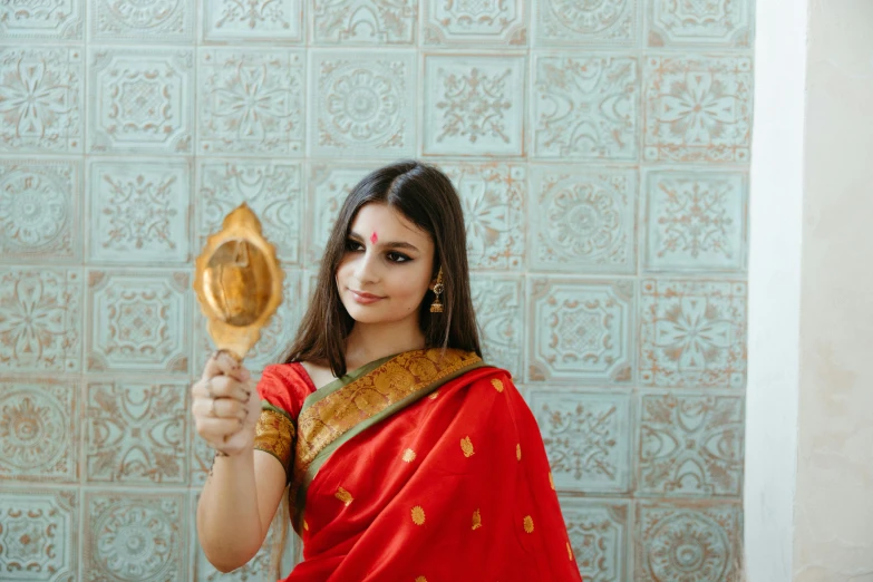 a woman in a red sari holding a mirror, pexels contest winner, hurufiyya, gold and red metal, teenage girl, (good looking ), deity)