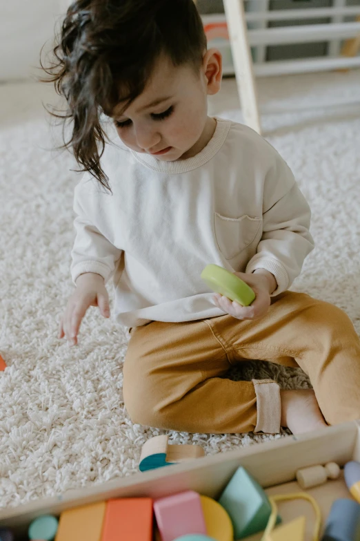 a little girl sitting on the floor playing with blocks, pexels contest winner, holding an avocado in his hand, beige, pants, organic shape