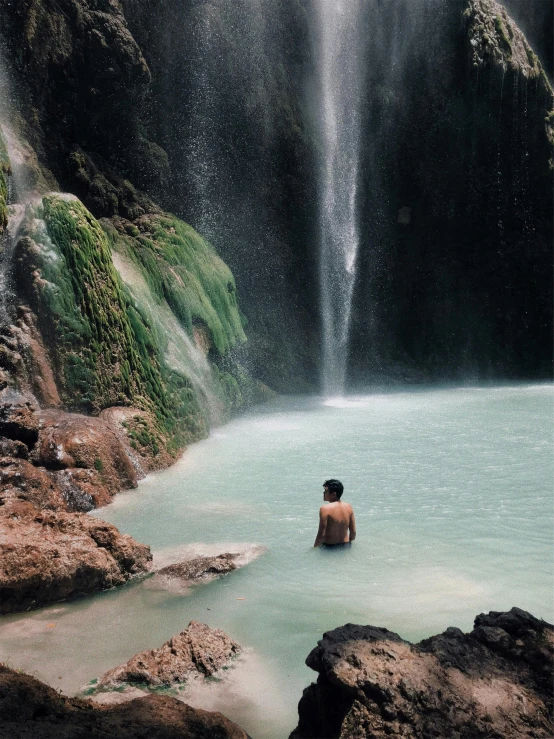 a man standing in front of a waterfall, by Jessie Algie, unsplash contest winner, sumatraism, sitting at the edge of pool, standing next to desert oasis, crystal clear neon water, green waters