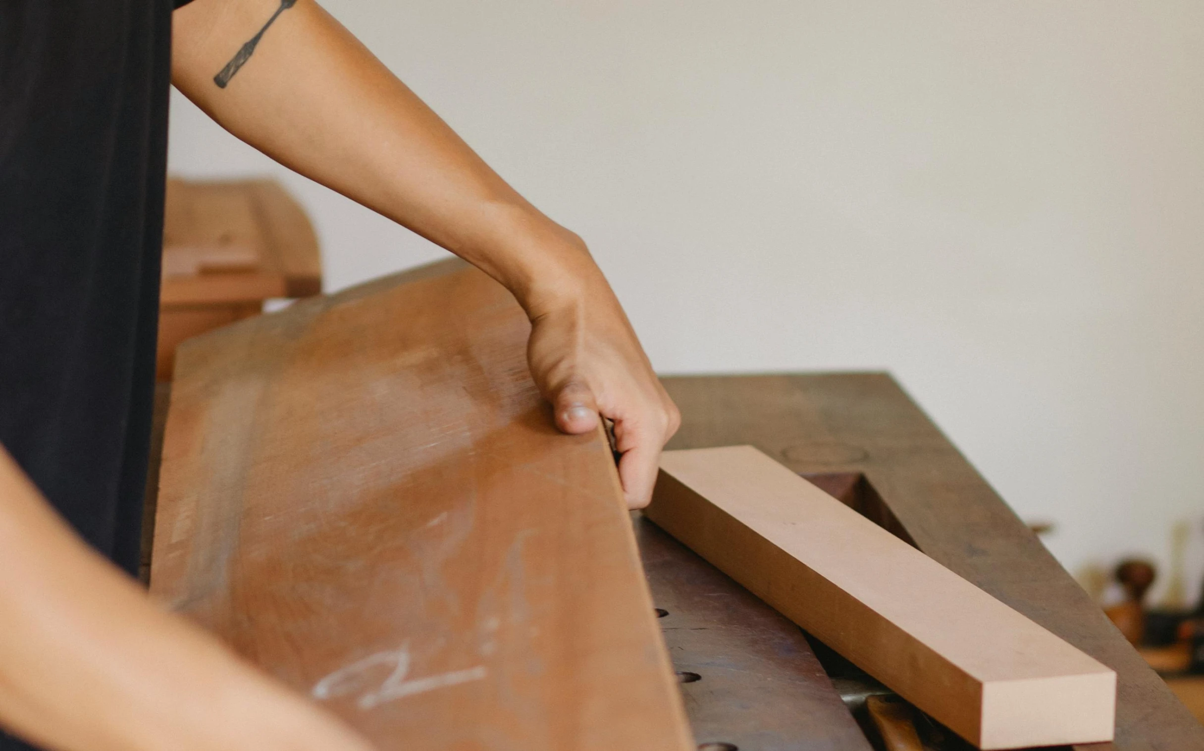 a person holding a piece of wood on top of a table, by Jessie Algie, trending on unsplash, arts and crafts movement, arched back, benches, leather padding, insisted on cutting in line