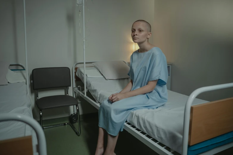 a person sitting on a bed in a hospital room, a portrait, pexels contest winner, antipodeans, partially bald, eleven/millie bobbie brown, gown, svetlana tigai