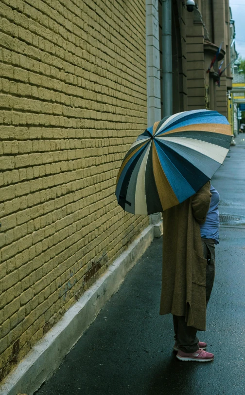 a person standing in the rain with an umbrella, a picture, inspired by Louis Stettner, unsplash contest winner, earth tones and blues, hiding behind a brick wall, on a sidewalk of vancouver, pointy conical hat