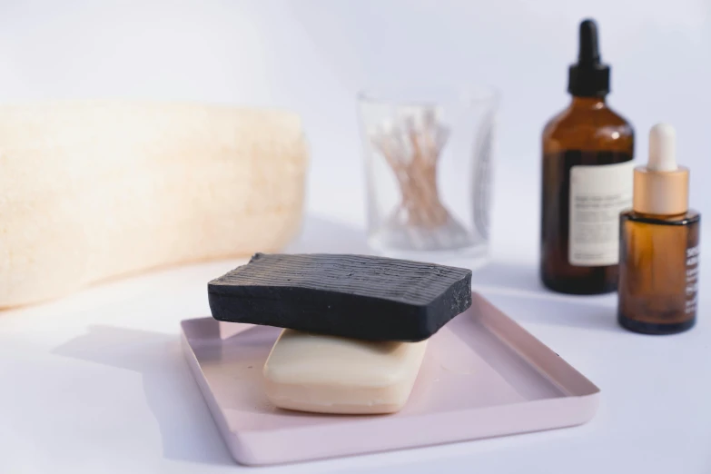 a couple of soap bars sitting on top of a pink plate, a picture, by Alice Mason, unsplash, all black matte product, square, black on white, ingredients on the table