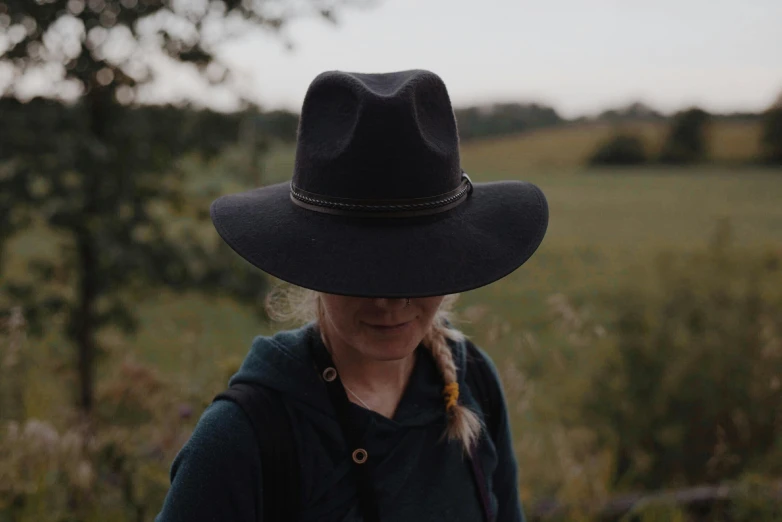 a woman wearing a black hat standing in a field, a picture, by Emma Andijewska, deerstalker, subtle detailing, midnight, handcrafted