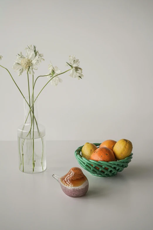 a vase filled with flowers next to a bowl of fruit, inspired by Elsa Beskow, unsplash, photorealism, pastries, minimalist photorealist, with celadon glaze, fruits in a basket