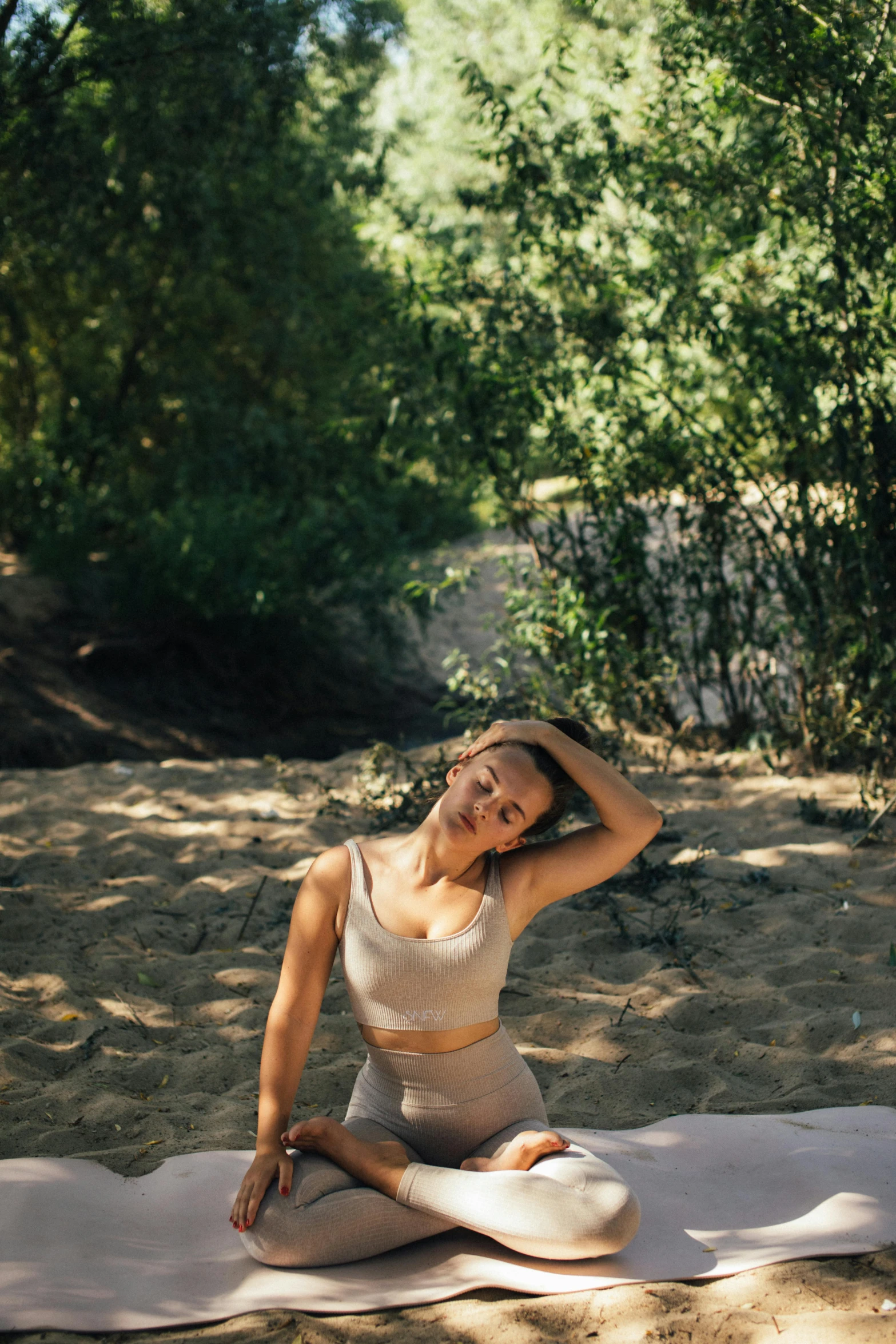 a woman sitting on a yoga mat in the woods, a picture, unsplash, graceful body structure, on the sand, sunny light, waving
