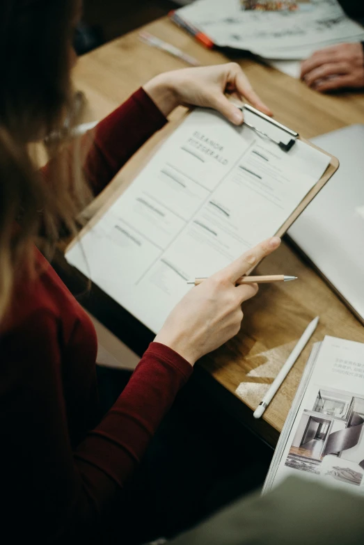 a woman sitting at a table holding a clipboard, pexels contest winner, blue print, detailed information, in house, sleek design