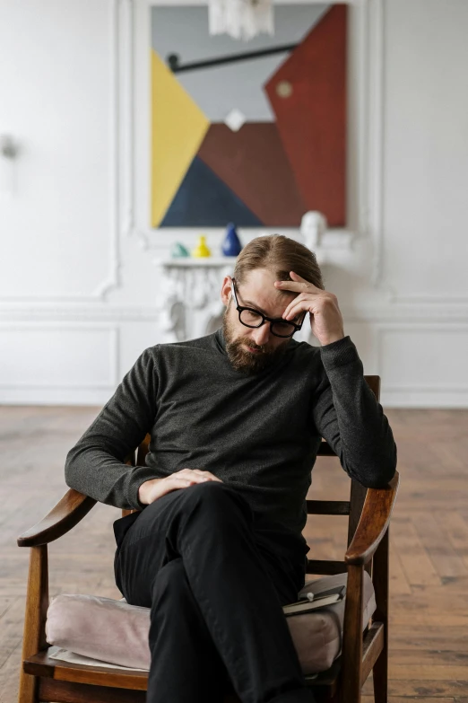 a man sitting in a chair talking on a cell phone, a minimalist painting, inspired by Constantin Hansen, pexels, visual art, ginger bearded man with glasses, looks sad and solemn, shot with sony alpha 1 camera, hammershøi