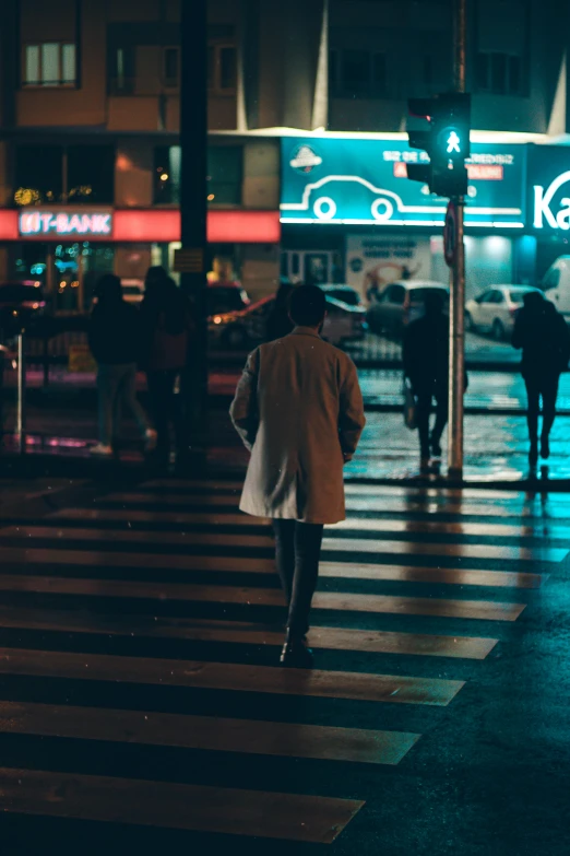 a person walking across a street at night, by Niko Henrichon, trending on unsplash, in a cybercity, wet floor on streets, promo image, nightlife