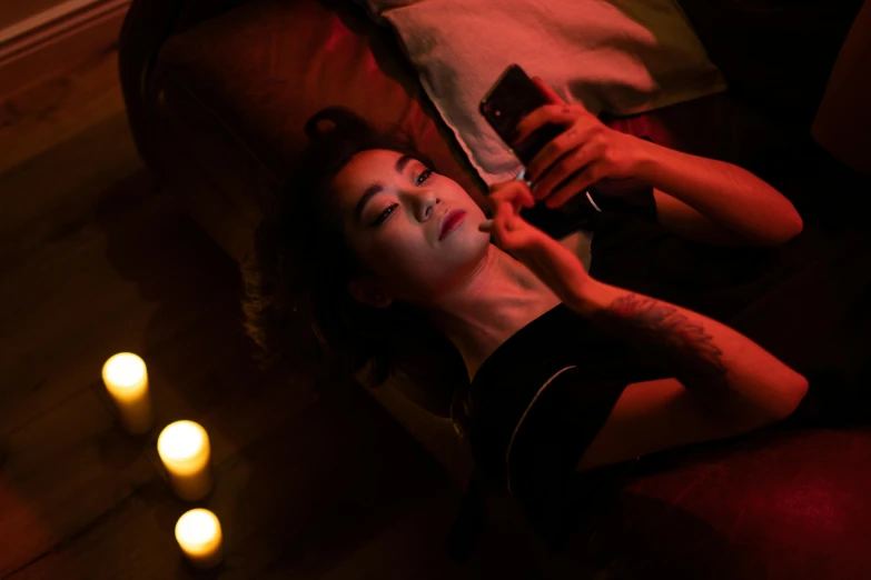a woman laying on a couch holding a cell phone, a portrait, inspired by Nan Goldin, trending on pexels, cozy dark 1920s speakeasy bar, of taiwanese girl with tattoos, laying in bed, rituals