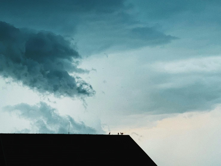 a group of people standing on top of a roof under a cloudy sky, a photo, unsplash contest winner, minimalism, evening storm, two stories, viewed from a distance, teal sky
